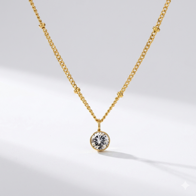 Diamond birthstone pendant necklace in gold-toned chain on cream background. By Sophi.