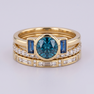 Stack of gold rings with blue gemstones and diamonds on a light gray background