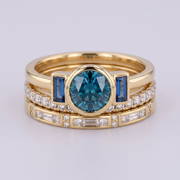 Stack of gold rings with blue gemstones and diamonds on a light gray background
