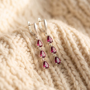 By Sophi Natural Rhodolite Garnet Drop Earrings, catalog flat-lay on warm cream wool