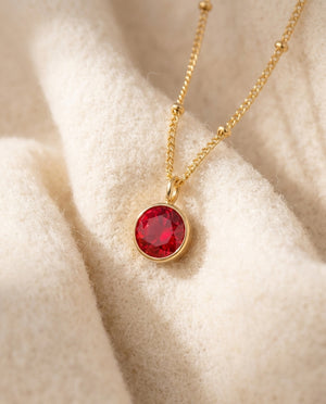 By Sophi Personalized Ruby Birthstone Pendant Necklace flat-lay on warm cream wool