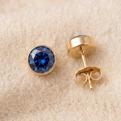 By Sophi Sapphire Birthstone Studs flat-lay on warm cream wool