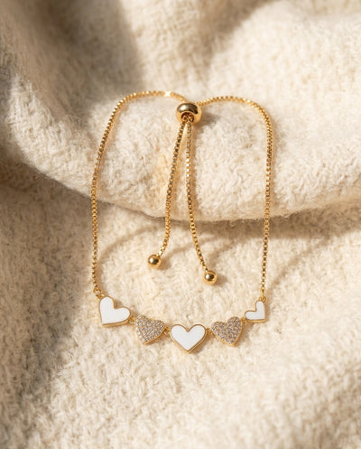 By Sophi White Enamel & Gold Heart Bracelet flat-lay on warm cream wool